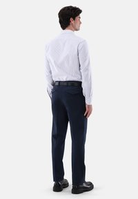 Weißes, vertikal gestreiftes Hemd mit klassischem Kragen, in marineblaue Hose gesteckt; schwarzer Gürtel und glatte schwarze Schuhe vervollständigen den Look.