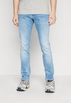 Jeans de mezclilla azul claro con un corte ajustado, que presentan una textura desgastada. Combinados con zapatillas deportivas grises y naranjas, que cuentan con una parte superior de malla.