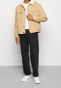 Beige manchesterjacka med vit fårskinnskrage, två bröstfickor, kombinerad med svarta jeans och vita sneakers.