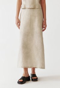 Beige linen maxi skirt with a simple design, paired with black clogs featuring a chunky heel and open toe. Smooth, lightweight texture.