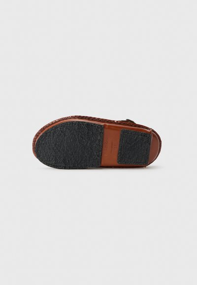 Semelle de chaussure en cuir marron avec caoutchouc noir texturé, forme courbée et bords cousus ; présente une base en cuir lisse et une petite zone en caoutchouc.