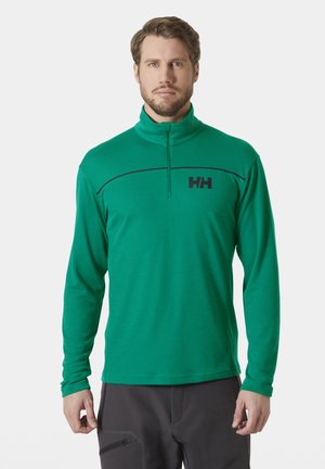 Camiseta activa verde de manga larga con cuello de media cremallera, que presenta una franja horizontal negra y un logo negro en el pecho. Fabricada en material ligero.