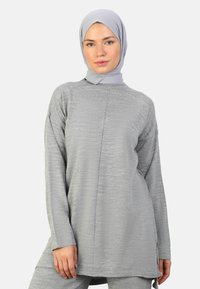 Light gray long-sleeve tunic with a textured finish, side slits, and a high neck. Paired with a matching gray hijab.
