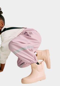 Pantalon étanche rose avec des bandes réfléchissantes, associé à des bottes en caoutchouc roses avec des semelles texturées et des panneaux élastiques sur les côtés.
