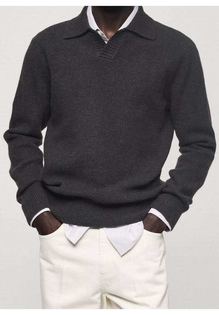Homme portant un pull côtelé gris foncé sur une chemise blanche à col, associé à un pantalon écru, les mains dans les poches.