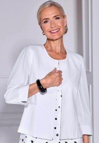 Witte gestructureerde blazer met een ronde halslijn, driekwart mouwen en een textiele stof. Accentueert met een zwarte bangle armband.
