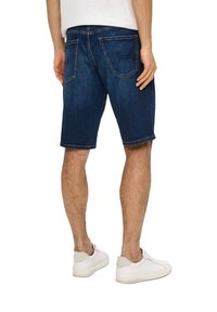 Shorts en denim bleu foncé, avec une coupe classique, des poches avant et arrière, et des coutures décoratives ; associés à des baskets blanches.