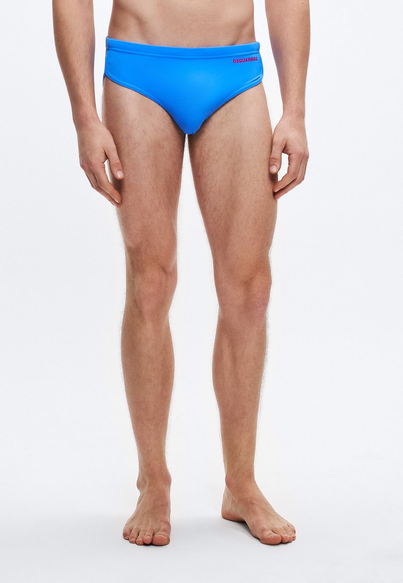 Μπλε ανδρικό μαγιό σε σορτς από απαλό ύφασμα, με σχέδιο χαμηλής μέσης και ελάχιστη κάλυψη. Ένα μικρό κόκκινο λογότυπο D Squared2 είναι ορατό στο μπροστινό μέρος.