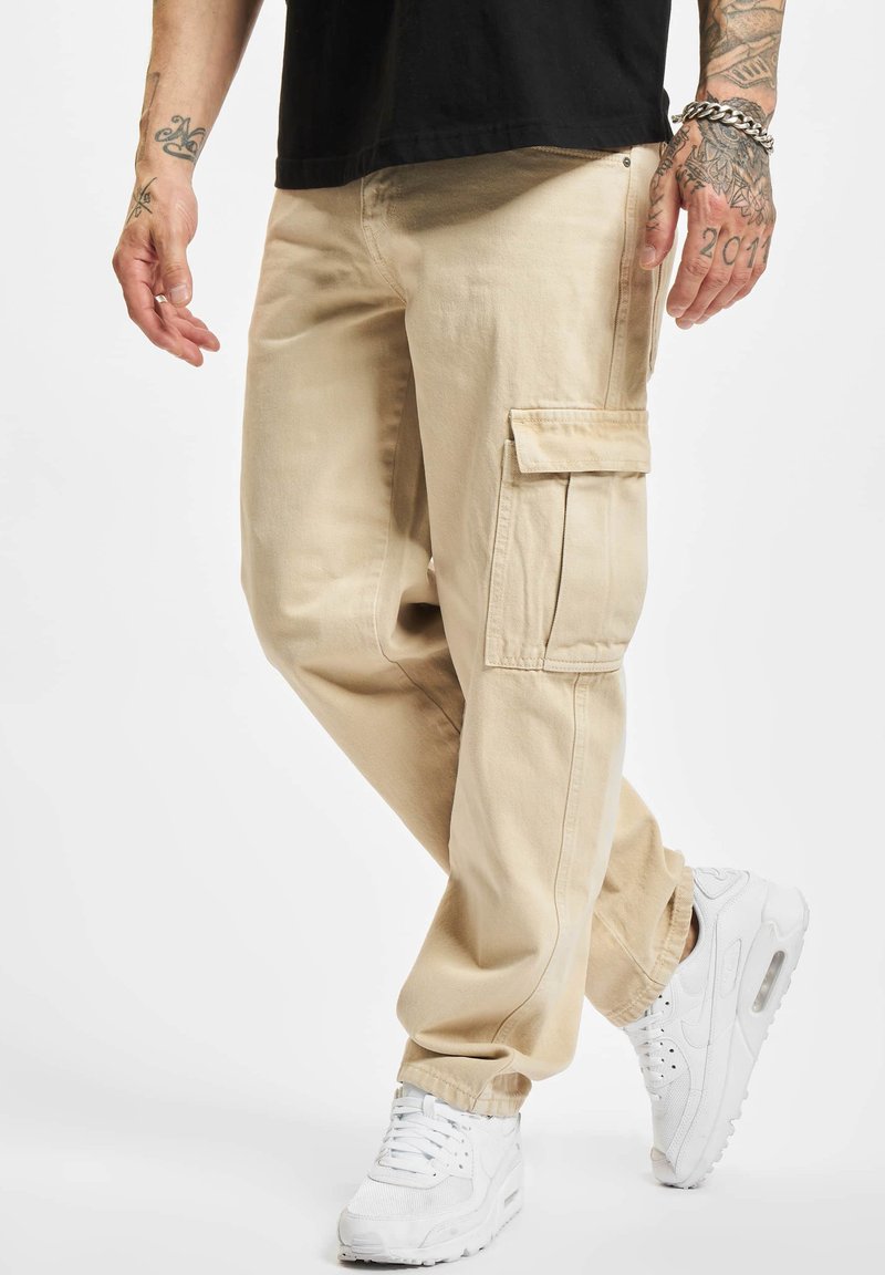 Beige cargo pants with multiple pockets and ankle cuffs, made from soft fabric. Paired with white athletic shoes.