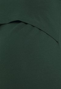 Vihreä lyhythihainen paita, jossa on kerroksellinen helma. Pehmeä ja sileä pinta, jolla on yksinkertainen muotoilu ja ompeluseparateet näkyvissä reunoilla.