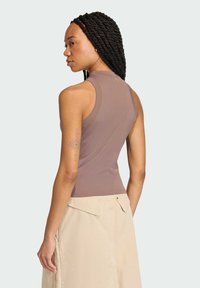 Brązowy top bez rękawów z wysokim dekoltem, zestawiony z beżową spódnicą. Gładka tekstura, dopasowany krój, minimalistyczny styl i brak widocznych wzorów.