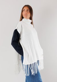 Poncho bianco lavorato a maglia con colletto alto, dotato di maniche blu scure e orlo frangiato. Texture morbida e vestibilità comoda, progettato per il massimo comfort.