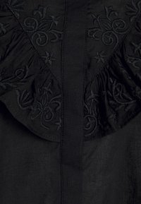 Tessuto nero ricamato con volant testurizzati e motivi floreali. Presenta una cucitura centrale e ricami intricati lungo il colletto.