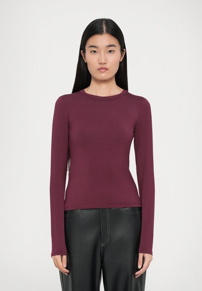 Top burdeos de manga larga con cuello redondo, ajustado, textura suave y detalles de costura mínimos, combinado con pantalones negros.