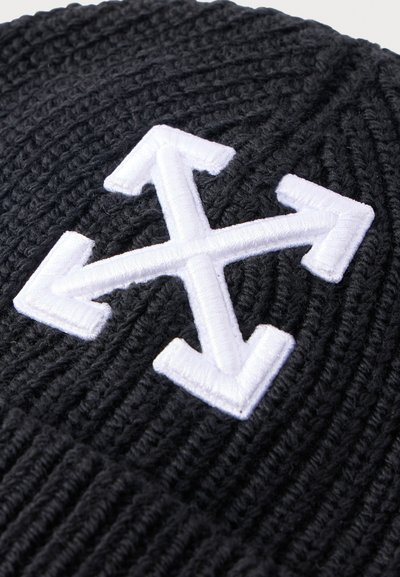 Tissu en tricot noir avec un motif brodé blanc représentant quatre flèches croisées pointant vers l'extérieur dans différentes directions.