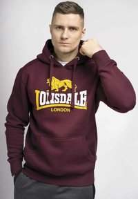 Felpa color bordeaux con logo di un leone giallo e testo bianco che recita "Lonsdale London." Presenta una tasca a marsupio frontale e cappuccio con cordino.