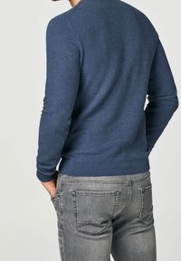 Navyblaues Strickpullover mit strukturierter Webart, gerippten Bündchen und Saum, getragen mit grauen Jeans. Die Rückansicht zeigt ein tailliertes Design.