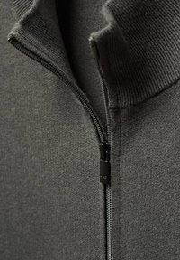 Pull gris foncé avec col zippé, bordures côtelées et tissu lisse texturé. Tirette de la fermeture éclair avec finition noire.