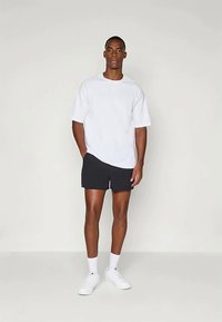 Balti trumpa rankovėmis marškinėliai, juodos šortai, balti sportbačiai, stovinčioje pozicijoje. Paprastas dizainas, lygus paviršius, neutralios spalvos, kasdieniškas įvaizdis.