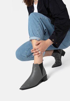 Stivali ankle in pelle grigia con punta a punta e tacco basso a blocco, dotati di pannelli laterali elasticizzati e superficie testurizzata, indossati con jeans arrotolati.