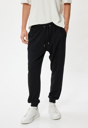 Sorte joggebukser med elastisk talje og snøre. Har ribbede afslutninger og en afslappet pasform. Bæres med hvide sneakers.