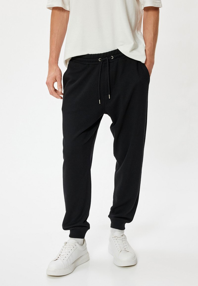 Sorte joggebukser med elastisk talje og snøre. Har ribbede afslutninger og en afslappet pasform. Bæres med hvide sneakers.