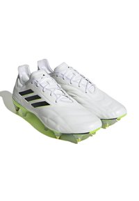 Scarpe da calcio bianche con design a tre strisce nere, parte superiore testurizzata, accenti gialli e tacchetti trasparenti, dotate di chiusura con lacci.