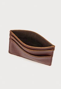 Καφέ δερμάτινη θήκη καρτών με υφή, διαθέτει τρεις θέσεις για κάρτες και διακριτικό κυρτό σχέδιο. Εσωτερικά επενδεδυμένη με σκούρο ύφασμα.