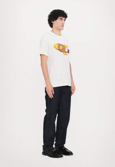 White cotton t-shirt featuring a yellow and brown rocket graphic. Worn with dark blue denim jeans and black shoes.