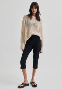Pull léger beige à côtes avec des manches surdimensionnées, associé à un pantalon noir cropped à la coupe ajustée et des sandales à lanières noires.