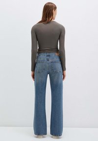 Maglietta a maniche lunghe grigia scura abbinata a jeans a vita alta di colore blu chiaro con gamba larga. I jeans presentano una patch in pelle e due tasche posteriori.