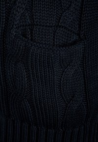 Mörkblå stickad tröja med en texturerad kabelmönster och ribbade fållar. Tillverkad av mjukt garn, vilket ger ett tjockt och mysigt utseende.