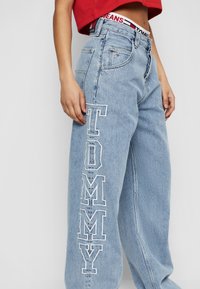 Světlé modré džíny s širokým střihem, s výraznou bílou výšivkou "TOMMY" na levém stehně a s logovaným páskem.