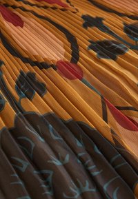 Pleated fabric with a floral pattern in warm tones of orange, brown, and teal. Features vertical lines and soft, textured surface.