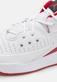 Scarpa sportiva bianca con tomaia in pelle sintetica, accenti in rete, suola in gomma rossa testurizzata e dettagli perforati per la traspirabilità.