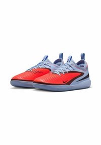 Las zapatillas deportivas Nike tienen un exterior rojo con surcos texturizados, acentos en azul claro y una suela gris. Los cordones y las lengüetas de agarre completan el diseño.