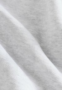 Világosszürke szövet lágy, texturált felülettel, finom árnyalatokkal és redőkkel. Az anyag könnyűnek és rugalmasnak tűnik.