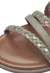Sanda de cuero marrón con tiras trenzadas grises, con acentos metálicos. Superficie suave y diseño de punta redonda, destacando los detalles de textura.