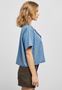 Lyseblå kortermet denimskjorte med krage, løs passform og synlige sømmer. Kombinert med mørkebrun shorts.