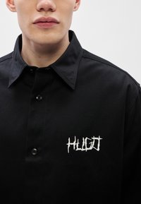 Μαύρο πουκάμισο με κουμπιά από βαμβακερό μείγμα, με κλασικό γιακά και κεντημένο λευκό λογότυπο "HUGO" στο αριστερό στήθος.