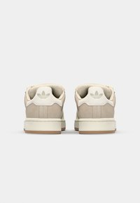 Sneakers in suede beige con suola in gomma piatta, caratterizzati da un design a tre strisce di un beige più chiaro e una linguetta sul tallone bianca con logo.