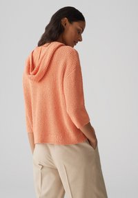 Felpa a maglia color corallo con finitura testurizzata, maniche a tre quarti e vestibilità comoda, abbinata a pantaloni larghi beige.