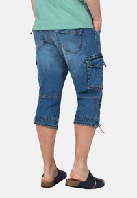Denim cargoshorts met knielange pasvorm, vervaagde blauwe kleur, meerdere cargozakken en contrasterende stiksels. Draagt met zwarte instapsandalen.