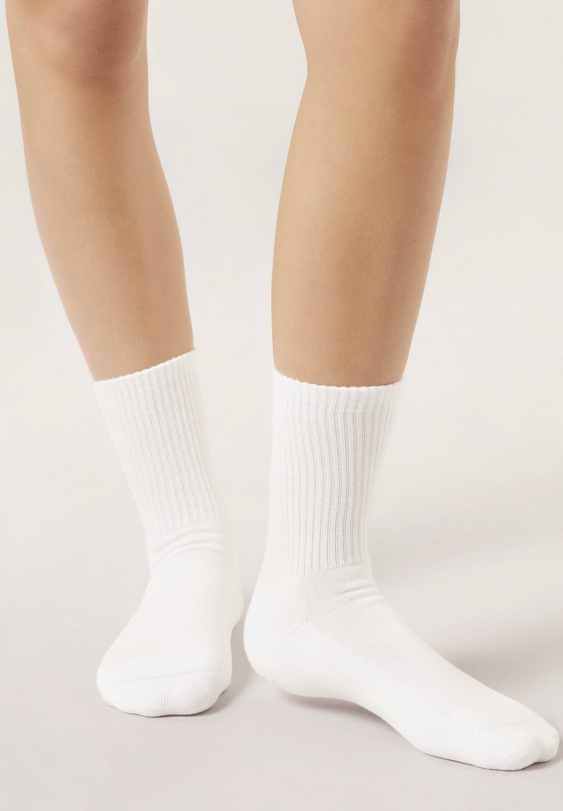 White cotton crew socks with ribbed texture and a smooth finish, reaching mid-calf, featuring a reinforced toe and heel.