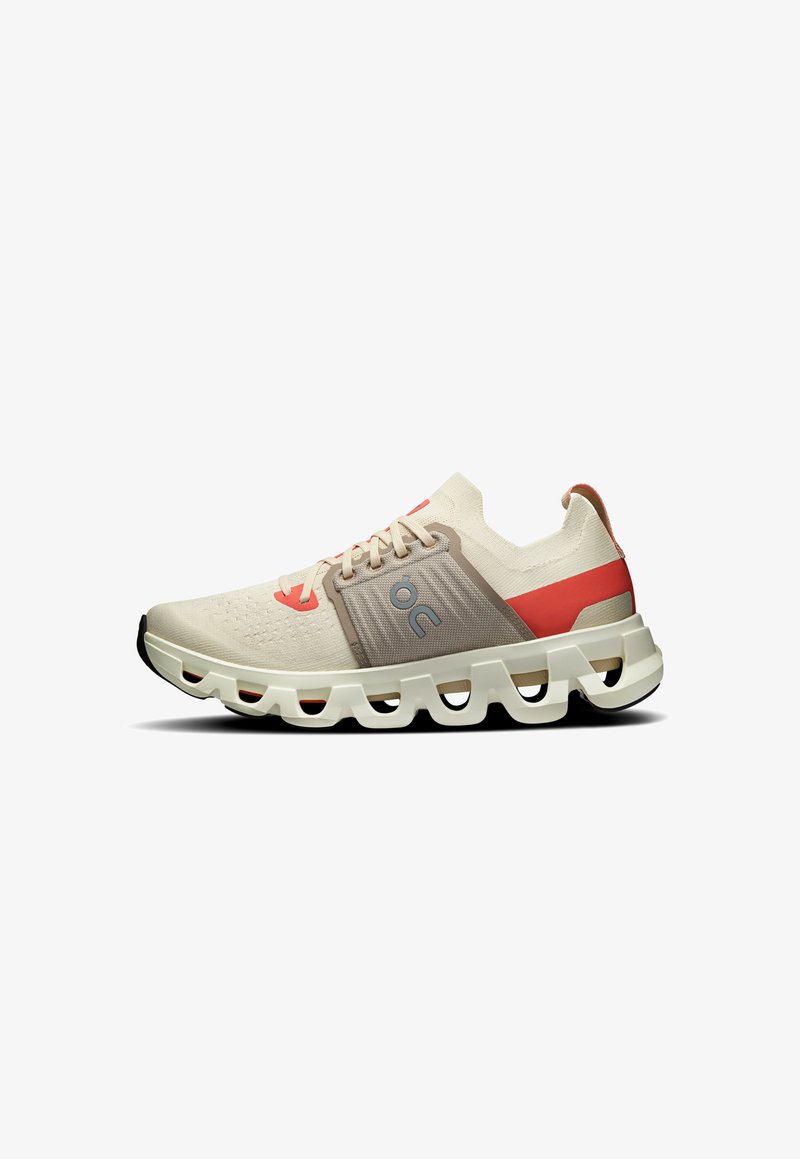 Baskets de sport beige avec un dessus texturé, des accents rouges et une semelle blanche épaisse comportant des sections découpées pour la respirabilité et la flexibilité.