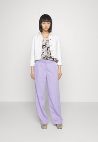 Casaco de ganga branco, blusa floral preta, calças largas lavanda e sandálias de plataforma verdes. Modelo está de pé contra um fundo simples.