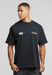 Svart bomull T-skjorte med korte ermer, med teksten "out of office" i hvitt og "Off Season" i gull broderi på forsiden.