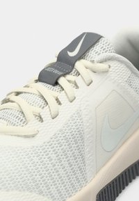 Ανοιχτό γκρι αθλητικά παπούτσια με ανώτερο υλικό από δίχτυ, υφασμάτινες επικαλύψεις και γκρίζα γλώσσα που διαθέτει λευκή ετικέτα "Just Do It". Μαύρη σόλα.