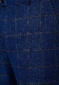 Niebieskie spodnie w kratę wykonane z teksturowanej tkaniny, z wzorem w kratę, z ciemnoniebieskimi i złotymi liniami oraz widoczną przednią kieszenią.