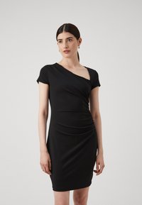Robe noire ajustée avec des manches courtes, encolure asymétrique et texture froncée d'un côté. Tissu lisse et extensible.